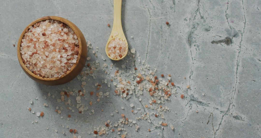 Displaying Coarse Himalayan Pink Salt in Wooden Bowl with Spoon on Stone Surface
