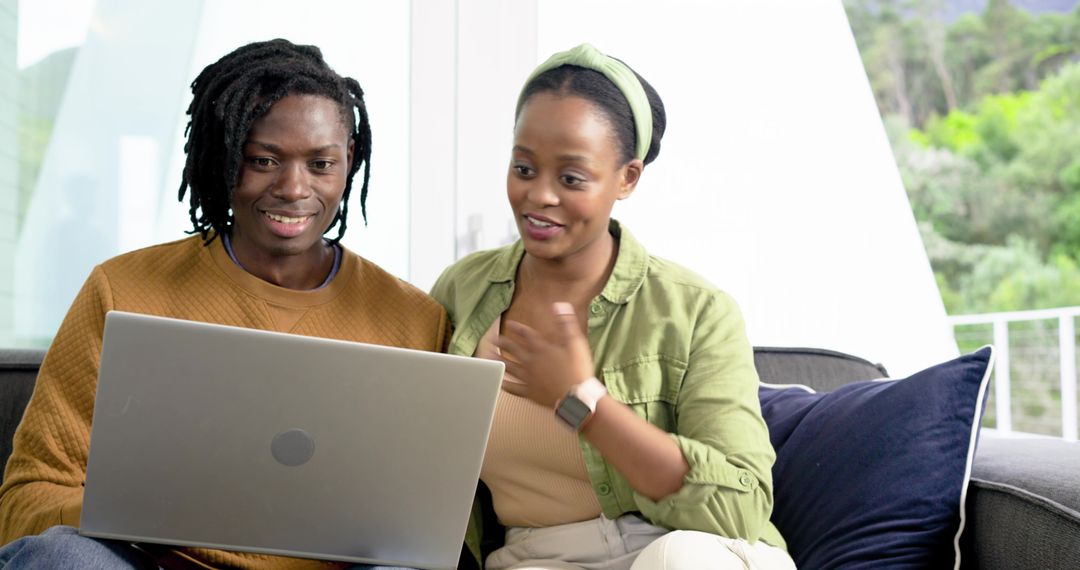 African American couple using laptop on sofa collaborating on project and planning at home