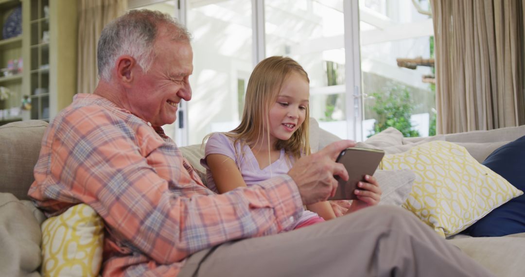 Grandfather and Granddaughter Laughing and Bonding on Couch with Tablet - Free Images, Stock Photos and Pictures on Pikwizard.com