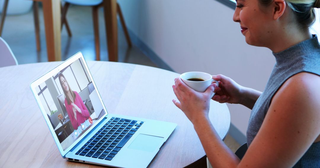 Woman Smiling While Video Calling and Holding Coffee Cup at Table - Free Images, Stock Photos and Pictures on Pikwizard.com