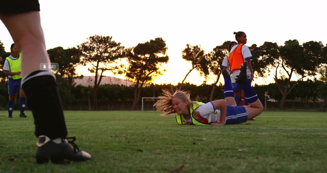 Blonde Female Soccer Player Falling and Grimacing During Sunset Practice on Grass Field