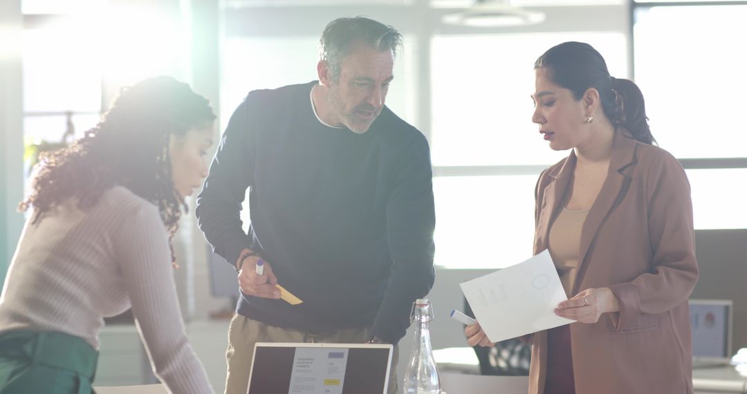 Diverse professionals collaborating around laptop and documents in bright modern office