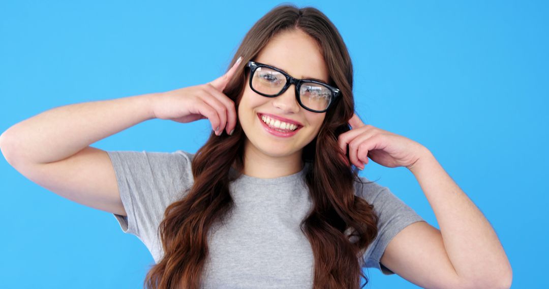 Cheerful Young Woman with Glasses Touching Her Ears Against Blue Background - Free Images, Stock Photos and Pictures on Pikwizard.com