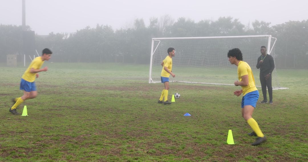 Soccer Team Training on Misty Field with Coach Conducting Drills