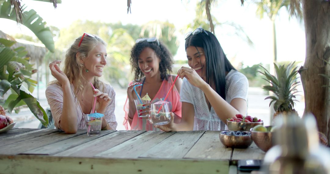 Young women enjoying tropical drinks at outdoor cafe - Free Images, Stock Photos and Pictures on Pikwizard.com