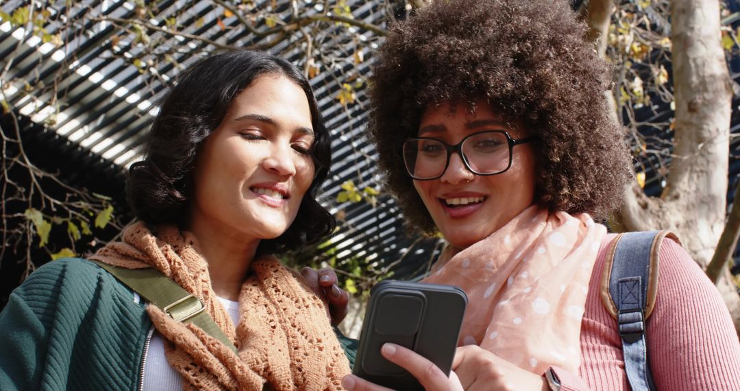 Friends sharing smartphone on campus laughing and pointing casual student lifestyle