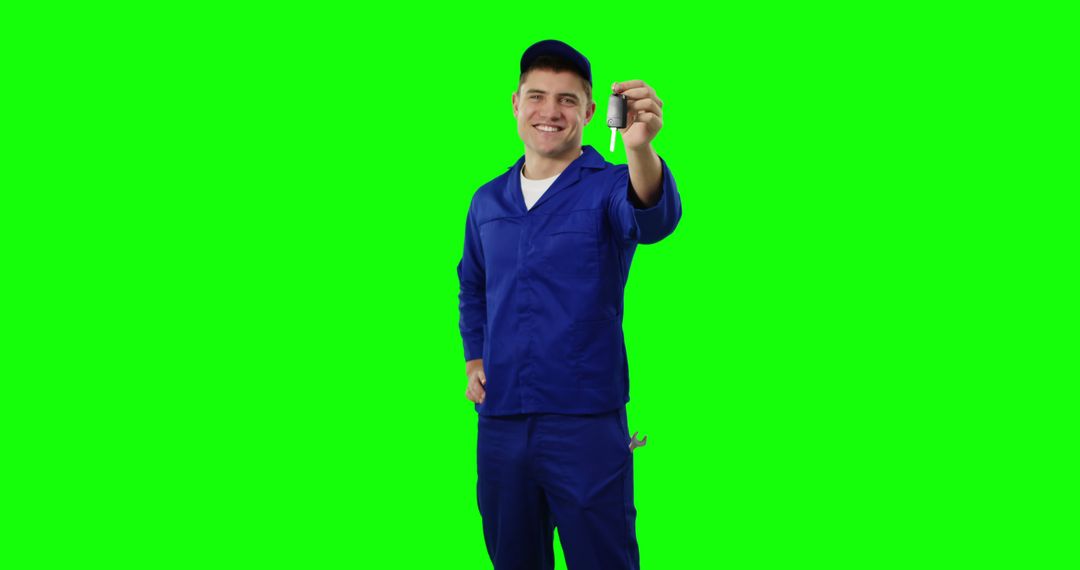 Smiling mechanic in blue overalls holding tool against green background - Free Images, Stock Photos and Pictures on Pikwizard.com