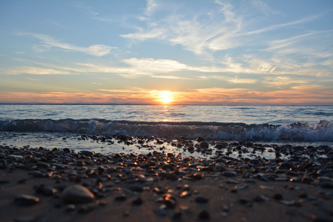 Serene beach sunset with calm waves and rocky shoreline - Free Images, Stock Photos and Pictures on Pikwizard.com