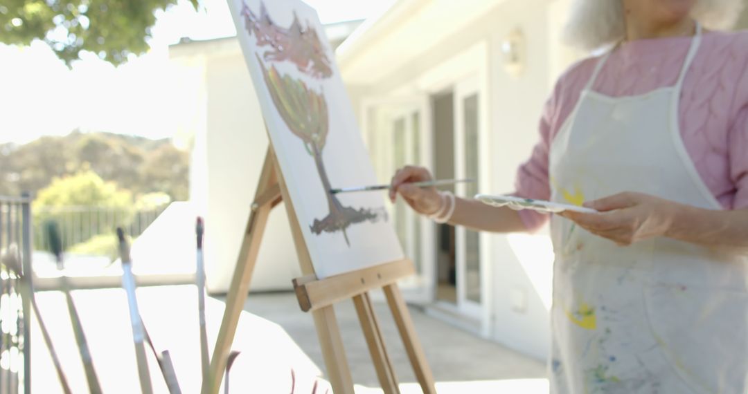 Senior Woman Painting on Canvas Outdoors in Sunlit Garden - Free Images, Stock Photos and Pictures on Pikwizard.com