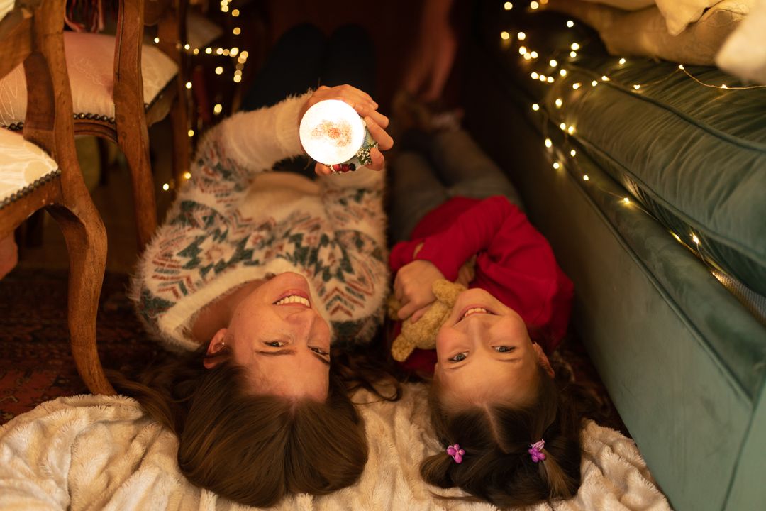 Mother and daughter bond in a lit blanket fort with a Christmas globe. - Free Images, Stock Photos and Pictures on Pikwizard.com