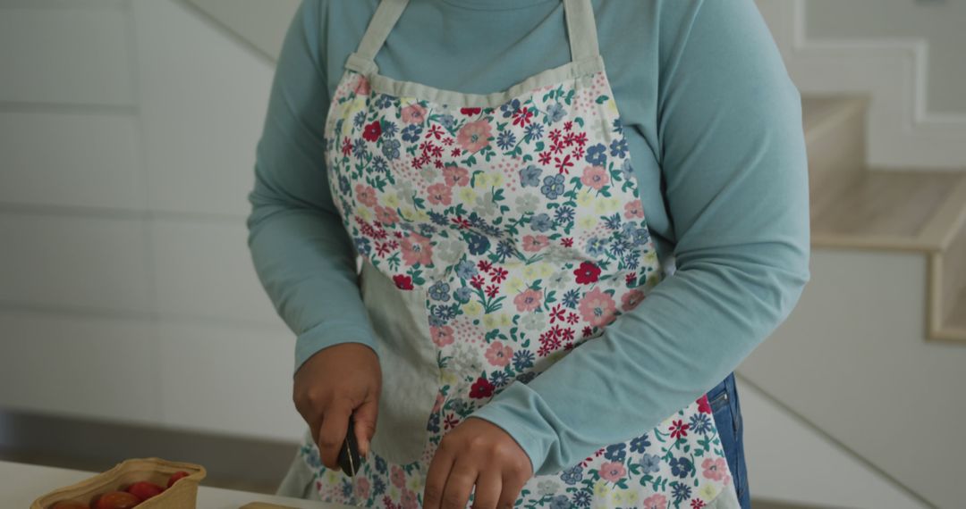 Woman wearing floral apron chopping vegetables in modern kitchen - Free Images, Stock Photos and Pictures on Pikwizard.com