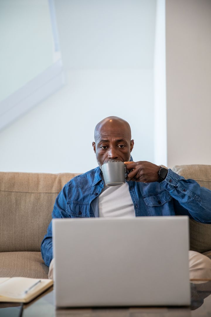 Man Drinking Coffee While Working on Laptop in Comfortable Living Room