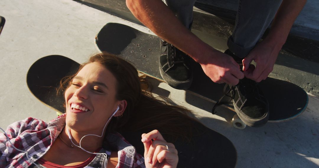 Happy caucasian woman using smartphone and man tying shoe at a skatepark - Free Images, Stock Photos and Pictures on Pikwizard.com