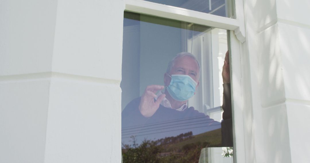 Senior Man Wearing Mask Waving from Window Indoors - Free Images, Stock Photos and Pictures on Pikwizard.com