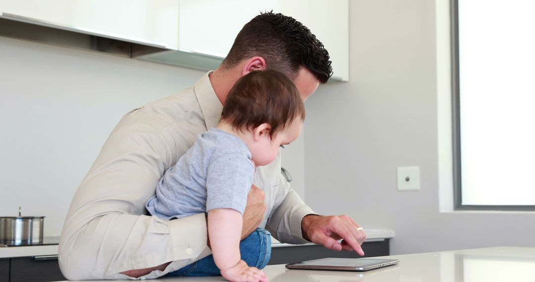 Father holding his baby before work and using tablet at home in the kitchen - Free Images, Stock Photos and Pictures on Pikwizard.com