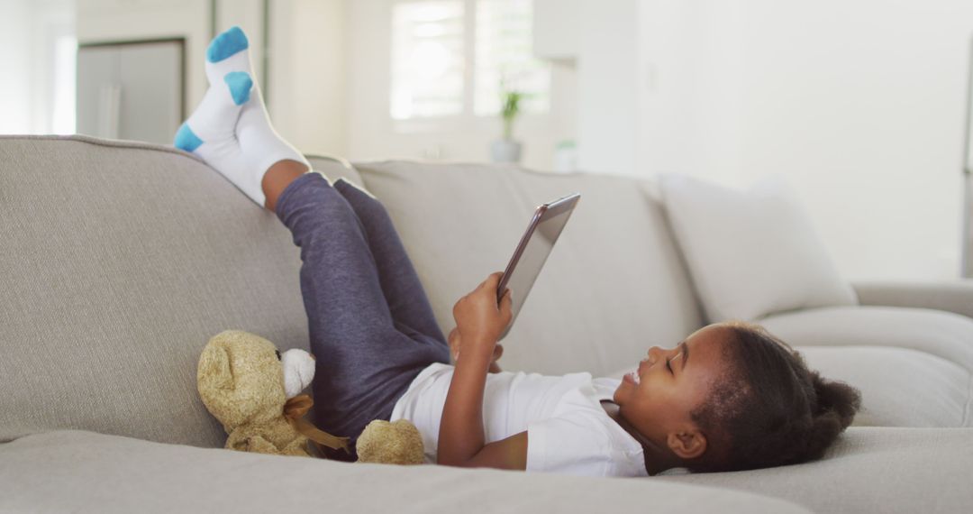 Young Child Relaxing on Couch with Tablet and Teddy Bear - Free Images, Stock Photos and Pictures on Pikwizard.com