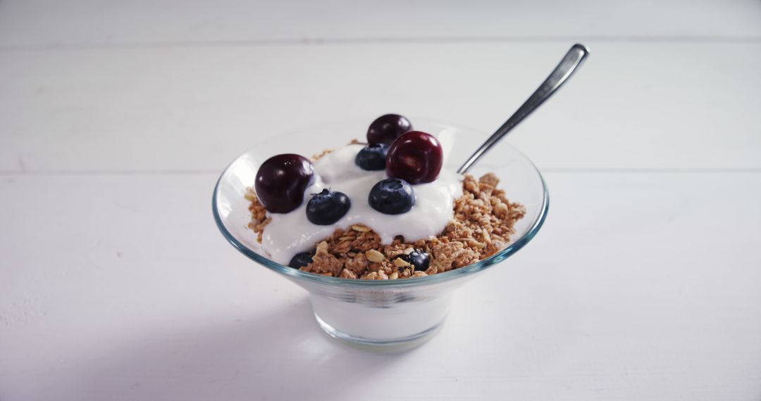 A bowl of yogurt with granola and fresh berries is served on a white surface, with copy space - Free Images, Stock Photos and Pictures on Pikwizard.com