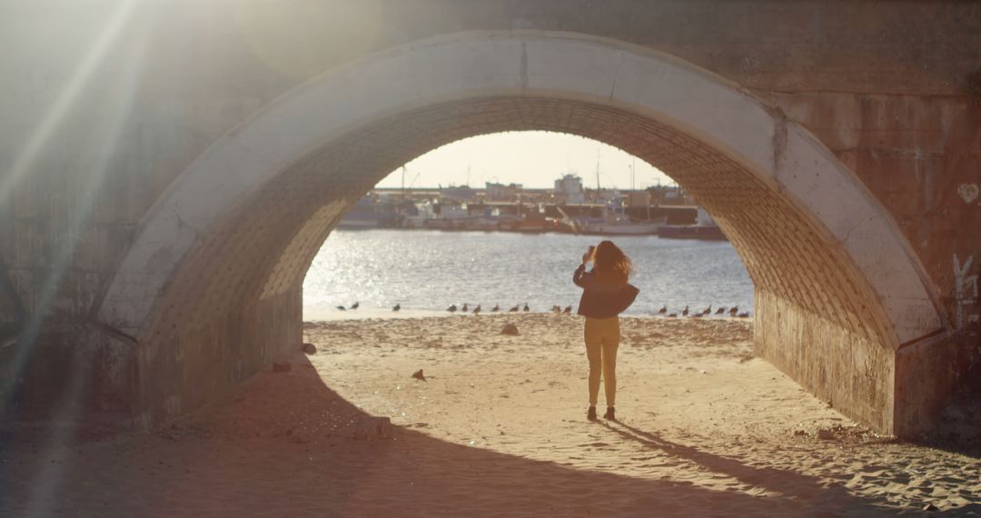 Woman Walking on Beach Under Bridge Arch During Sunset - Free Images, Stock Photos and Pictures on Pikwizard.com