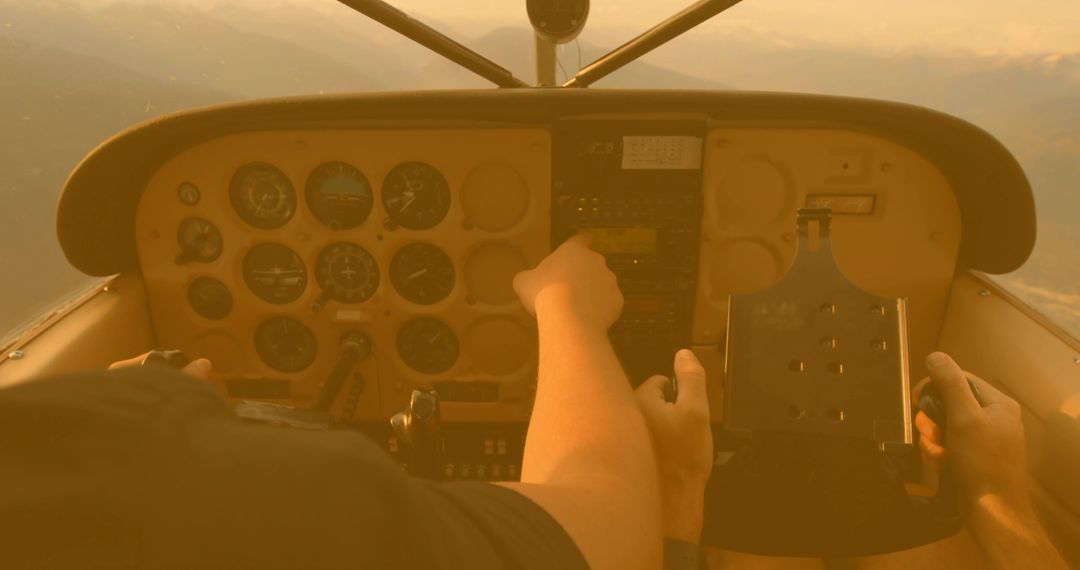 Pilots adjusting cockpit controls during golden-hour flight over mountains with avionics
