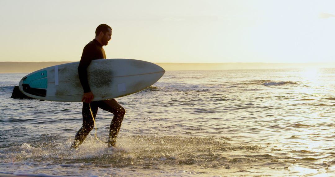 Surfer Carrying Board Across Shoreline at Sunset - Free Images, Stock Photos and Pictures on Pikwizard.com