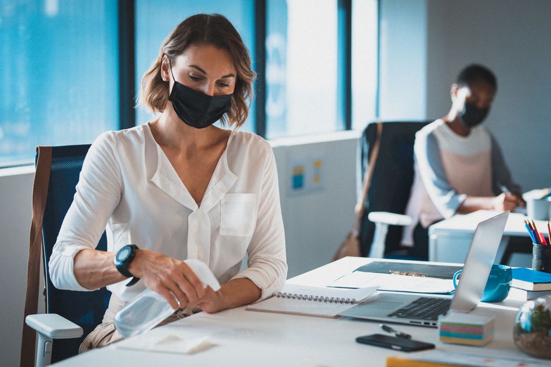 Two diverse businesswomen wearing face masks sitting in office, one disinfecting her desk - Free Images, Stock Photos and Pictures on Pikwizard.com