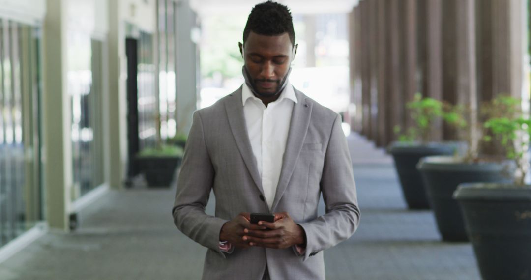 Young African American Businessman Using Smartphone in Modern Office Corridor - Free Images, Stock Photos and Pictures on Pikwizard.com