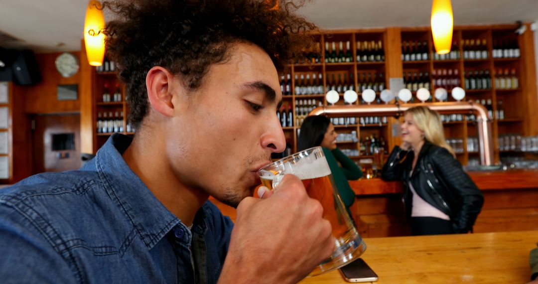 Young man enjoying beer in lively pub atmosphere - Free Images, Stock Photos and Pictures on Pikwizard.com