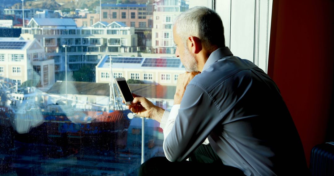 Mature Businessman Contemplating Through Office Window with Smartphone - Free Images, Stock Photos and Pictures on Pikwizard.com