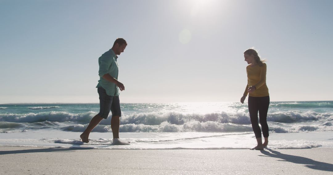 Couple Enjoying Walk Along Sunny Beach Shoreline - Free Images, Stock Photos and Pictures on Pikwizard.com