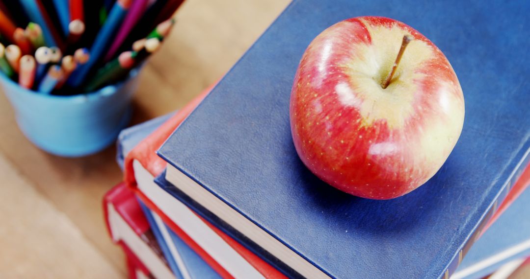 Red Apple on Stack of Books with Colorful Pencils at Classroom Desk