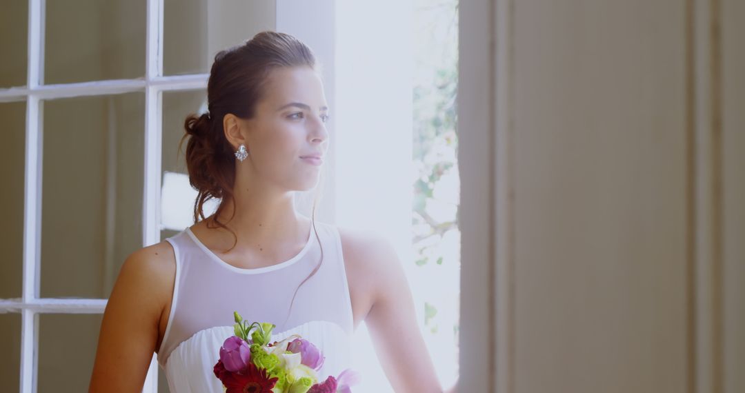 Bride with Bouquet Standing by Window in Sunlight