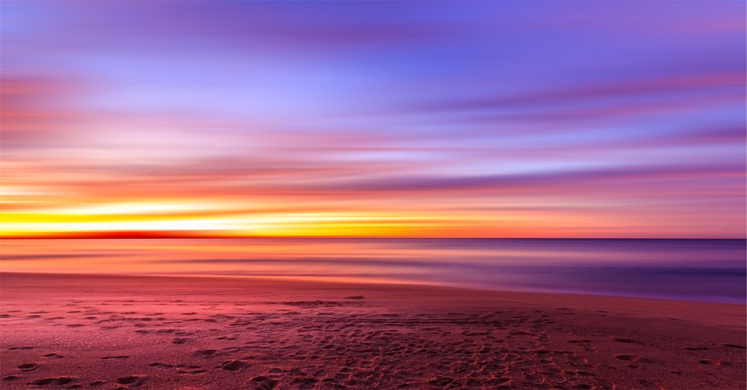 Long-Exposure Sunset Glowing Over Tranquil Beach with Colorful Sky and Footprints