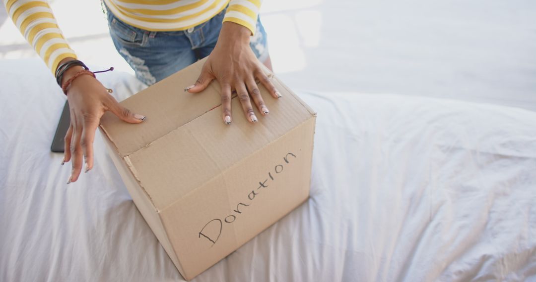 Person Viewing Donation Box on Bed in Bright Room