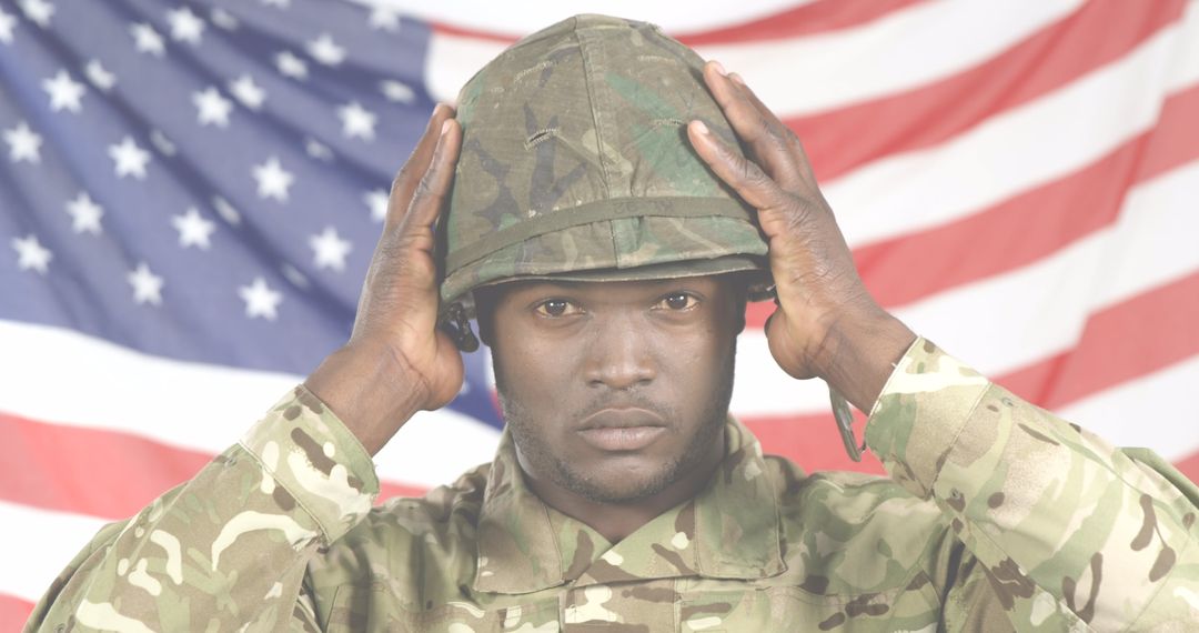 Soldier in Camouflage Adjusting Helmet with American Flag Backdrop