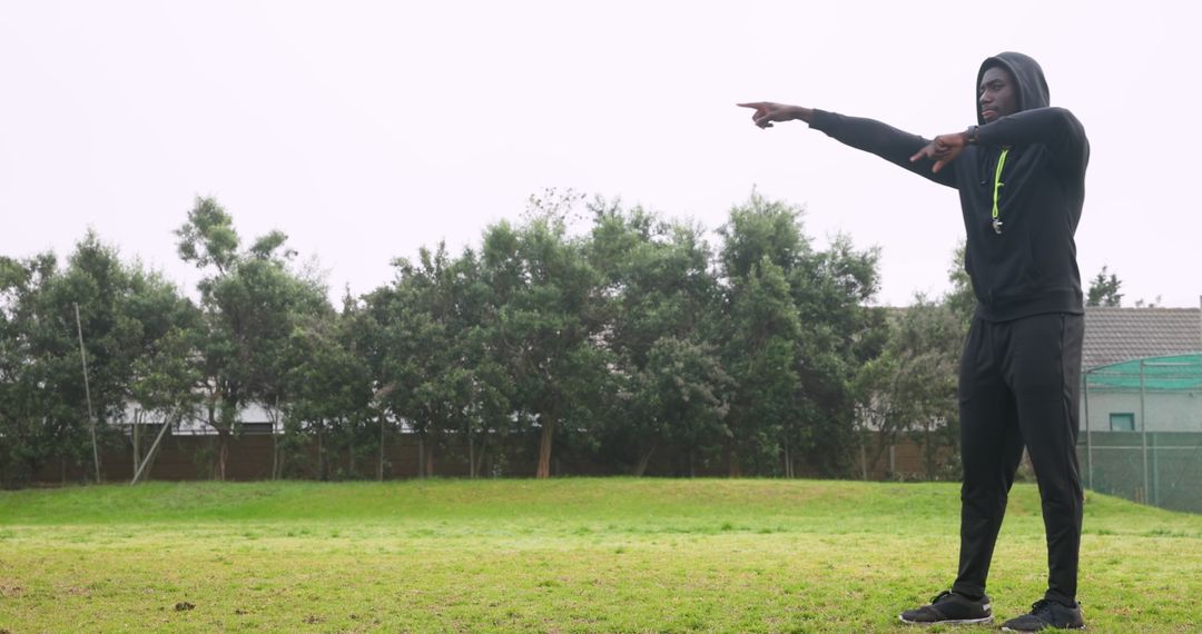 Athlete in Hoodie Pointing on Field with Trees in Background