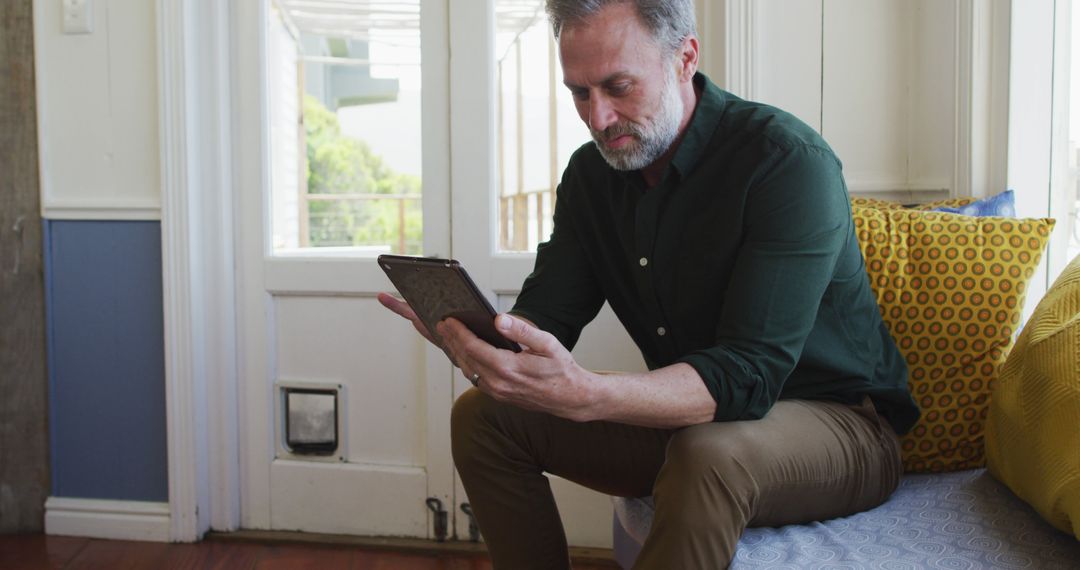 Middle-aged man reading tablet on modern sofa indoors - Free Images, Stock Photos and Pictures on Pikwizard.com