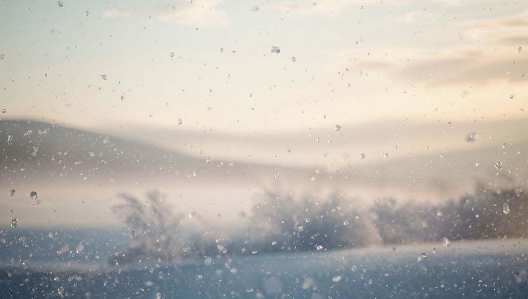 Water droplets on frosted window framing blurred snowy field and distant hills at sunrise