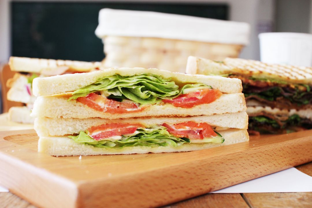 Stacking fresh tomato and lettuce sandwich on white bread on wooden board for lunch