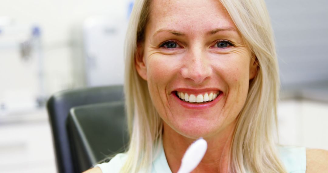 Smiling Blonde Woman in Dental Clinic Holding Toothbrush - Free Images, Stock Photos and Pictures on Pikwizard.com