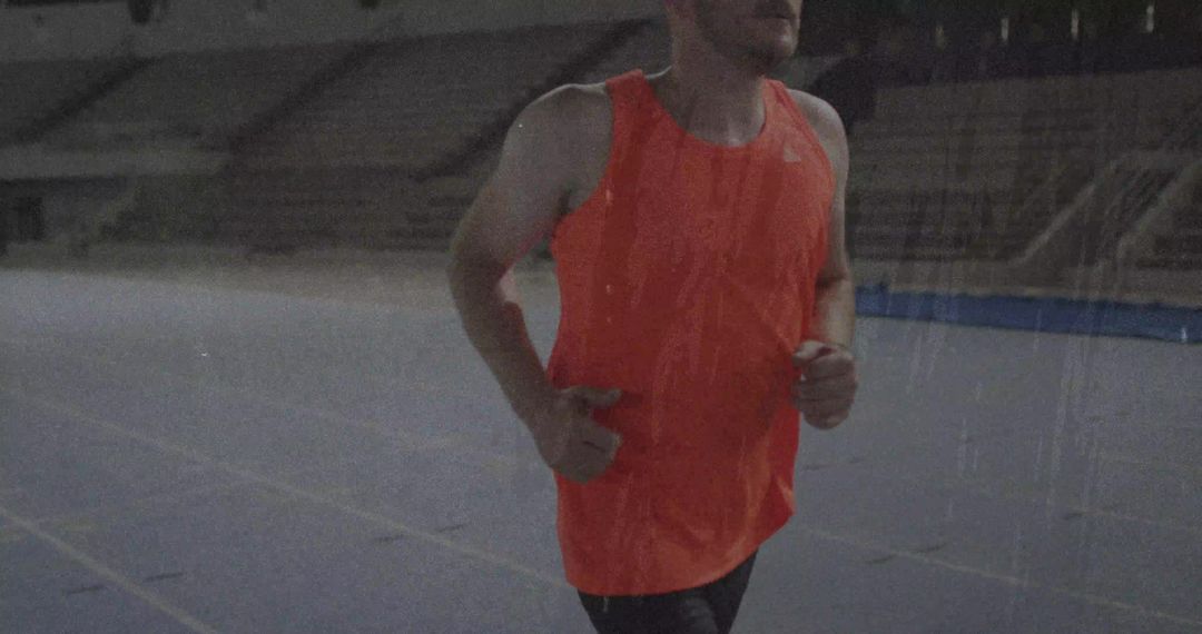 Athlete Running on Track in Empty Stadium in Orange Gear
