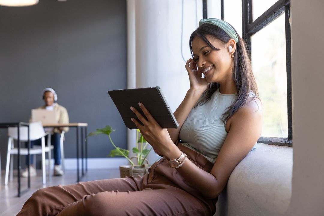 Smiling young professional using tablet while working at window in modern coworking space