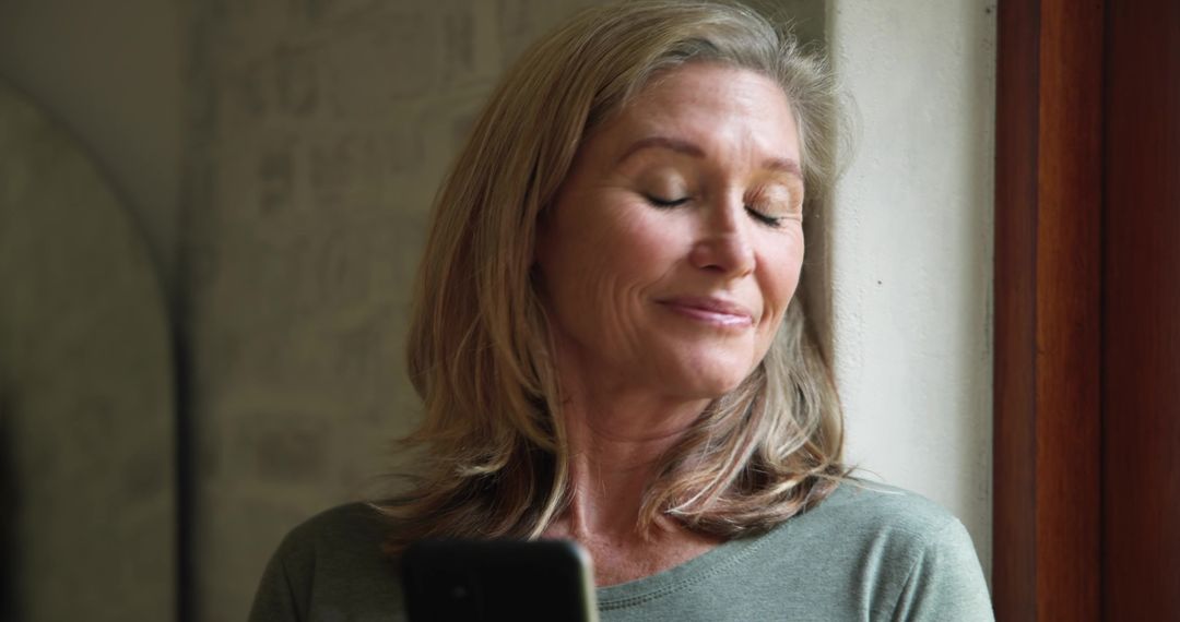 Mature Woman Relaxing by Window with Smartphone at Home