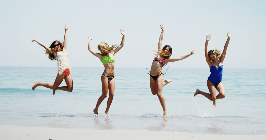 Four friends exude summer joy while leaping on a beach under a clear blue sky. - Free Images, Stock Photos and Pictures on Pikwizard.com