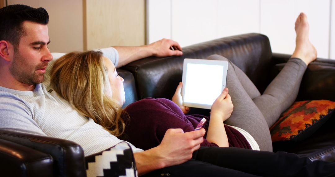 Couple Relaxing on Sofa Browsing Devices at Home