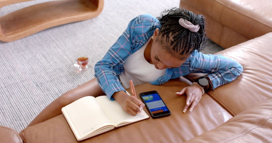 Woman Taking Notes Using Smartphone for Planning on Cozy Leather Couch