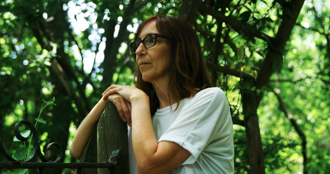 Thoughtful Woman Leaning on Gate in Forest surrounded by Green Nature - Free Images, Stock Photos and Pictures on Pikwizard.com