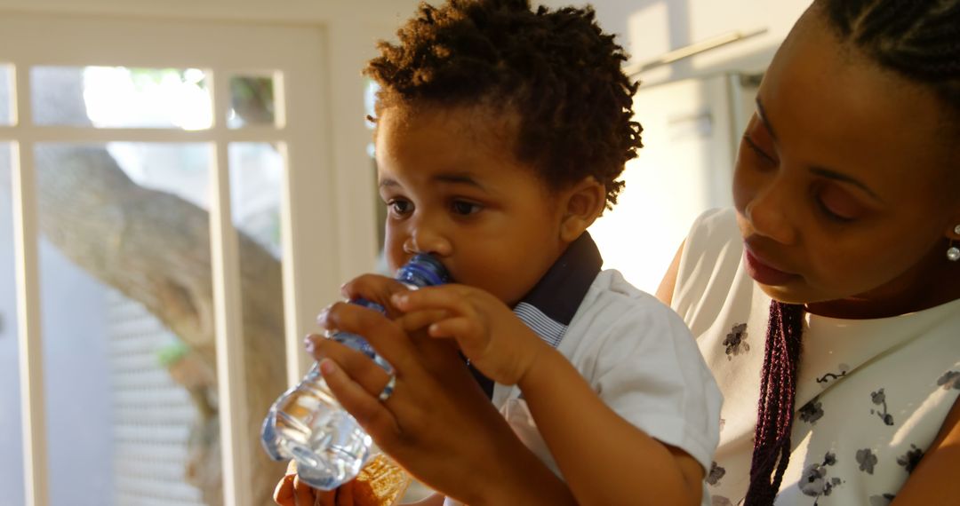 Caring Mother Helping Toddler Drink Water from Bottle in Sunlit Room - Free Images, Stock Photos and Pictures on Pikwizard.com