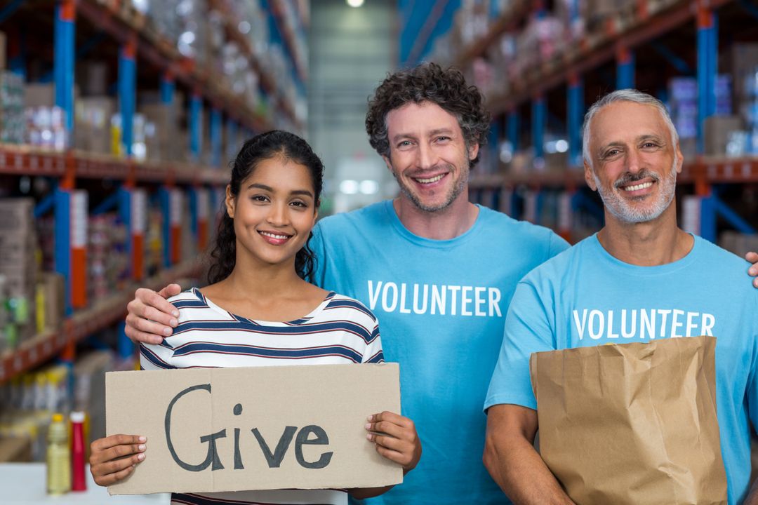 Happy Volunteers Holding Give Sign in Warehouse - Free Images, Stock Photos and Pictures on Pikwizard.com
