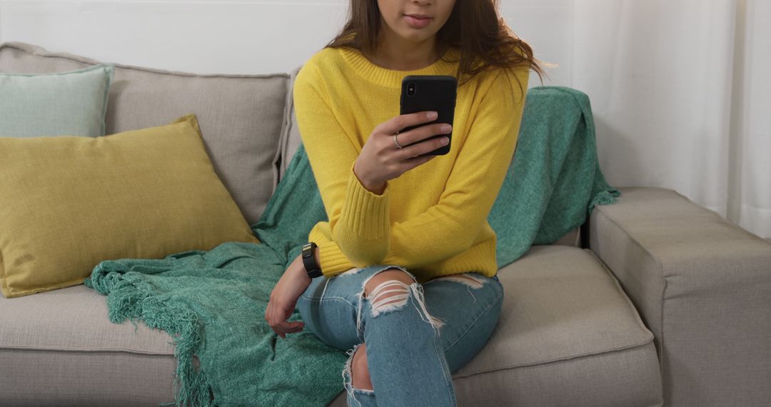 Young Woman Sitting on Sofa Using Smartphone in Cozy Living Room - Free Images, Stock Photos and Pictures on Pikwizard.com