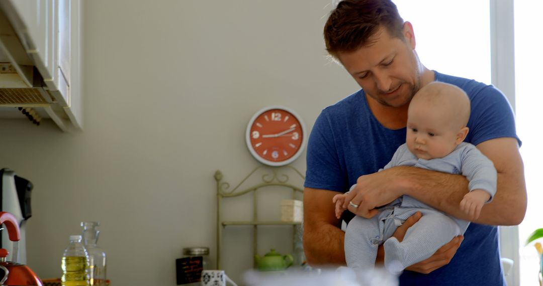 A middle-aged Caucasian man holds a baby in a cozy kitchen setting, with copy space - Free Images, Stock Photos and Pictures on Pikwizard.com
